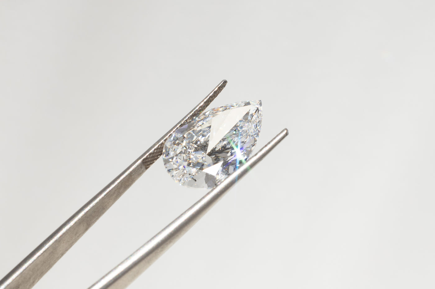 A 4 carat pear shaped diamond, held in a pair of jewellery tweezers.  
