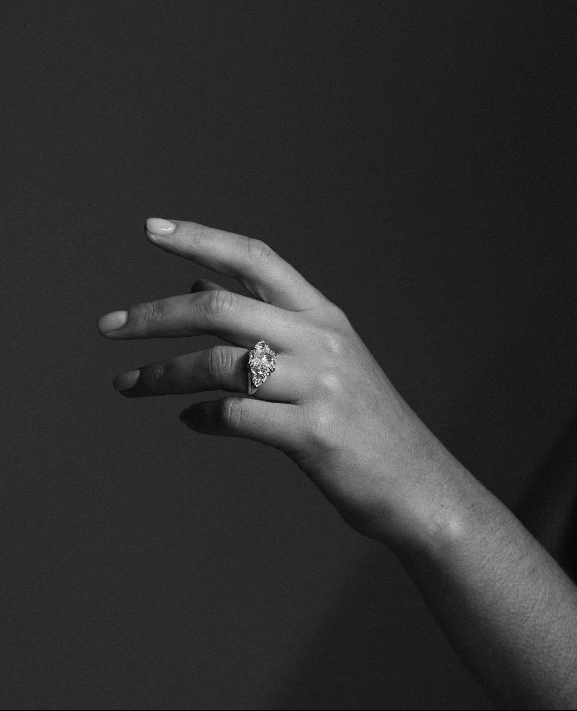 Hand wearing a large diamond engagement ring with a dark background. Handmade in Auckland, New Zealand