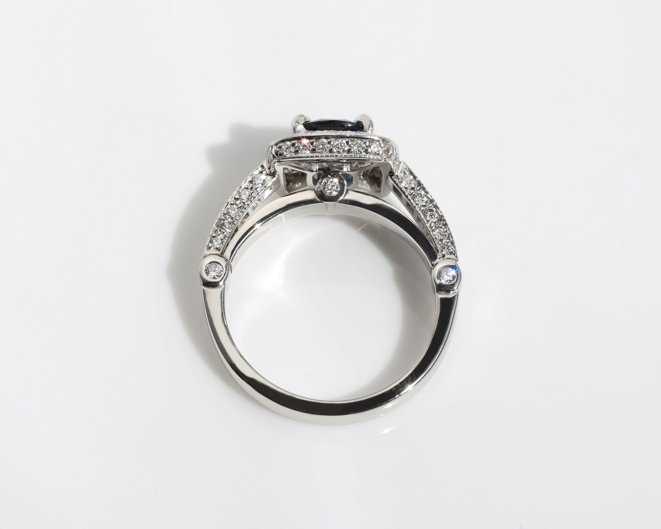 Handmade ring featuring a blue sapphire centre stone, surrounded by a halo of diamonds, with a pavé diamond band.