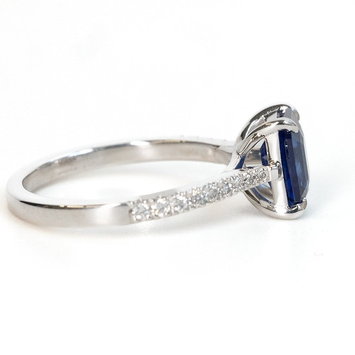 side veiw of an emerald cut blue sapphire ring with a pave diamond band, set in white gold.