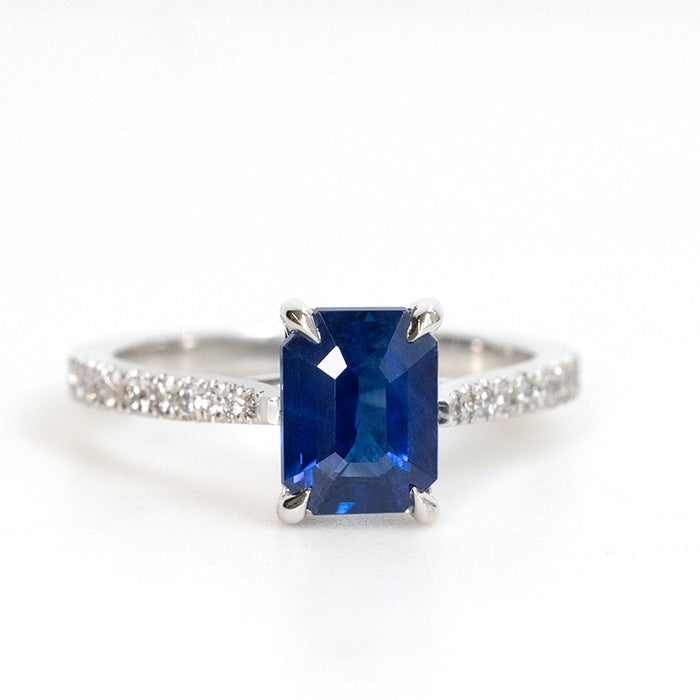 An emerald cut blue sapphire ring with a pave diamond band, set in white gold.