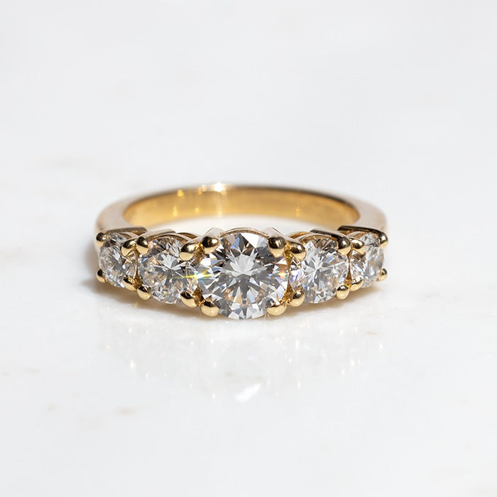 A five stone diamond ring with a central diamond flanked by four smaller diamonds, set in 18k yellow gold.