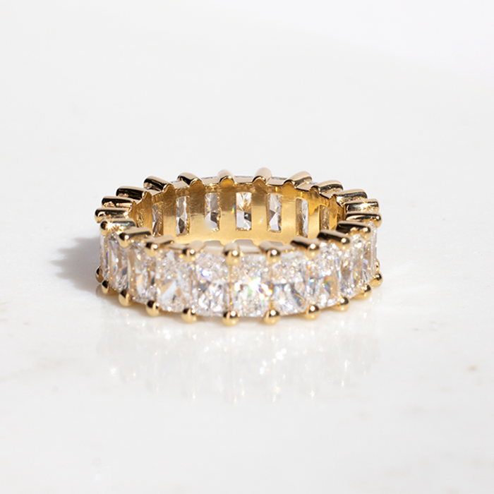 A luxurious diamond eternity ring with a circle of radiant-cut diamonds set in gold bands, placed on a marble surface.