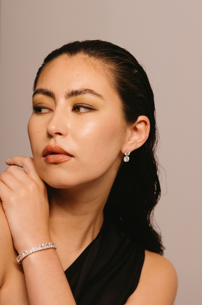 Model wears diamond drop earrings and large diamond tennis bracelet.