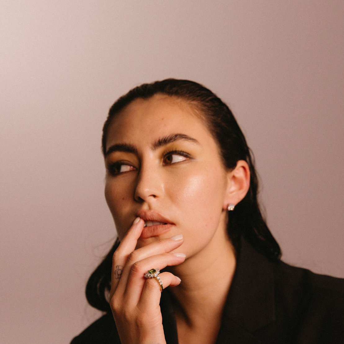 Model wears an asymmetric tsavorite and diamond ring with a gold band on her pinky finger
