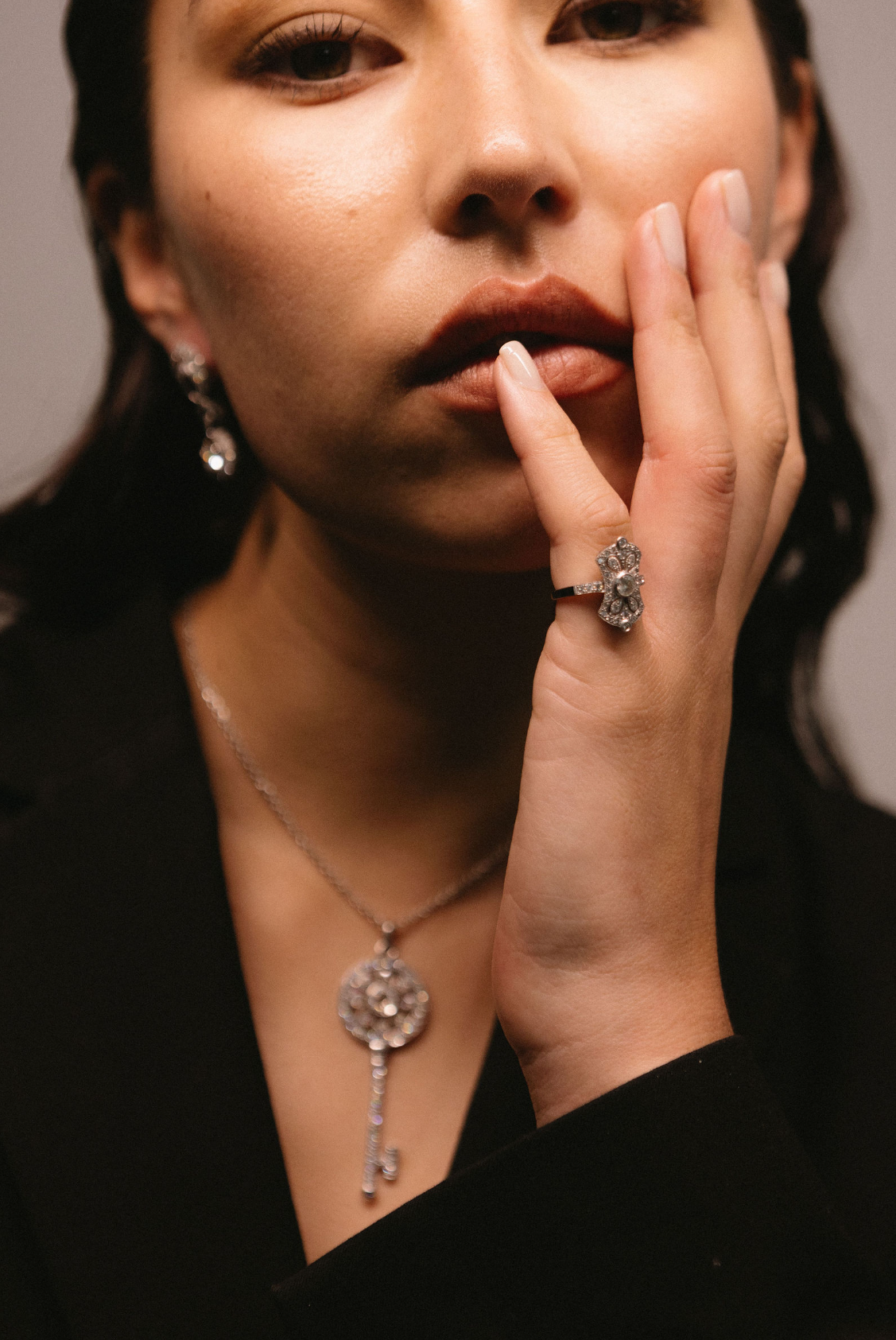 Model wears art deco ring with key pendant necklace and diamond drop earrings