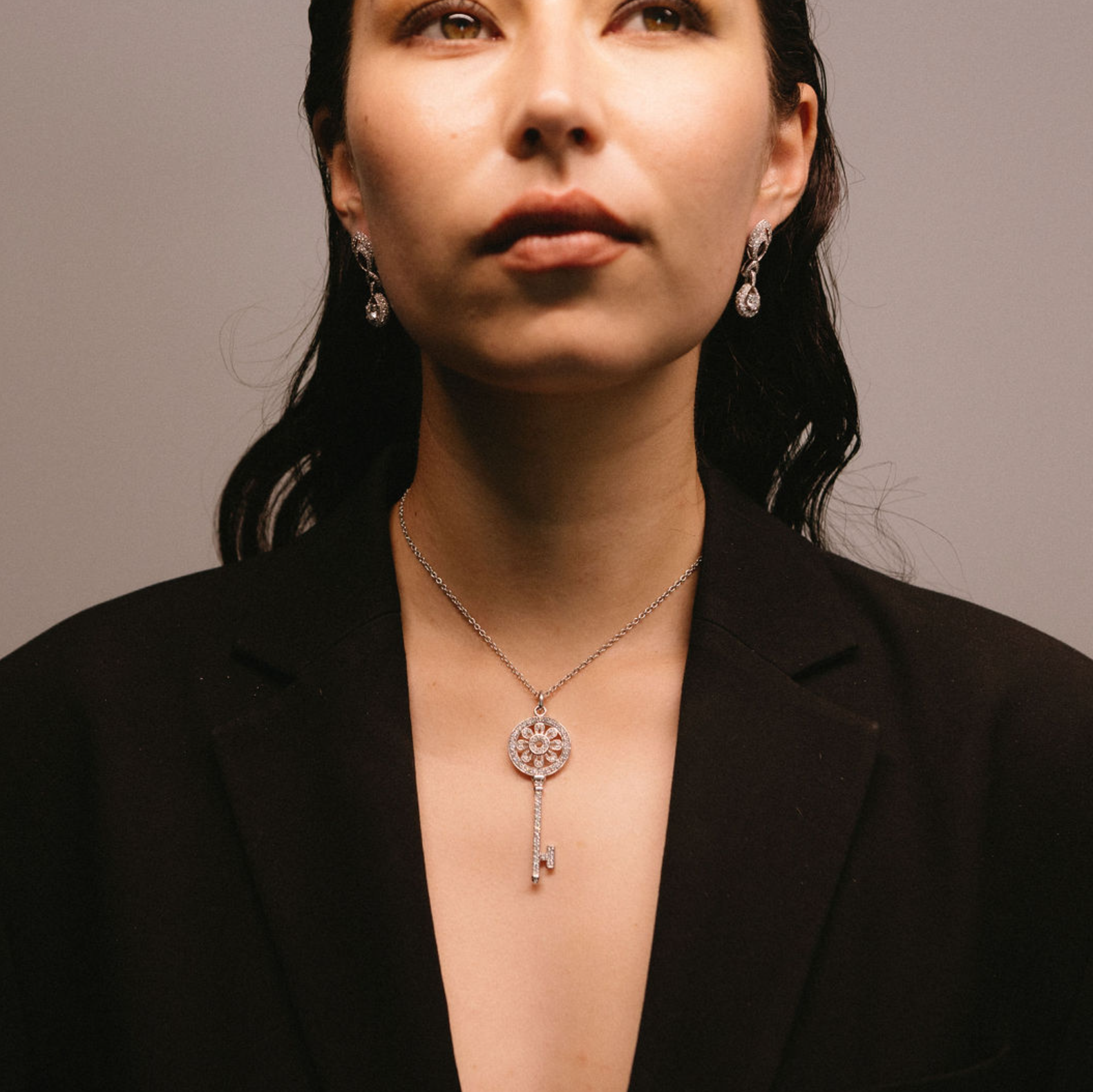 model wearing A white gold pendant necklace with a key design and diamond accents and matching diamond earrings.