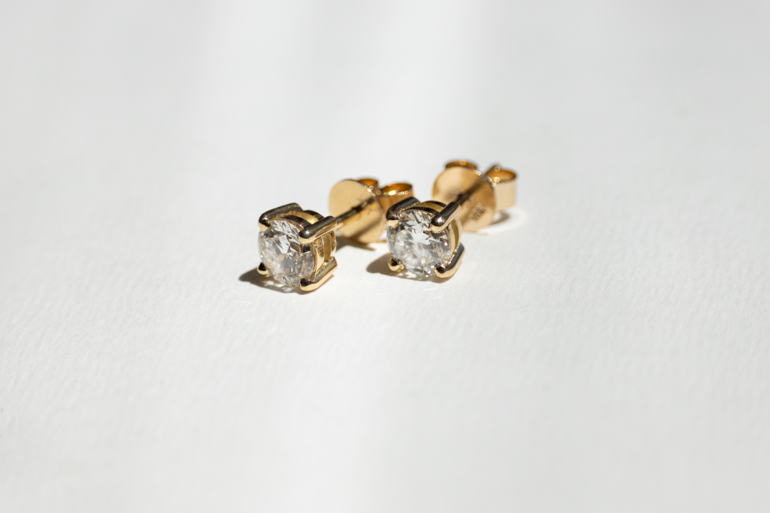 A pair of 18K yellow gold diamond stud earrings on a white background.