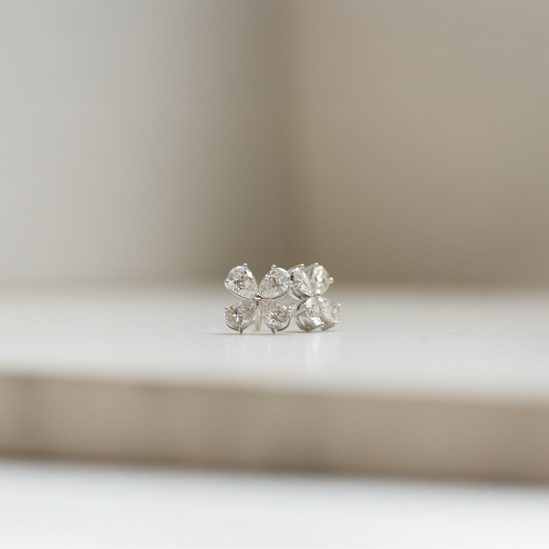 A pair of diamond stud earrings with a floral motif, displayed on a white surface with a soft background.
