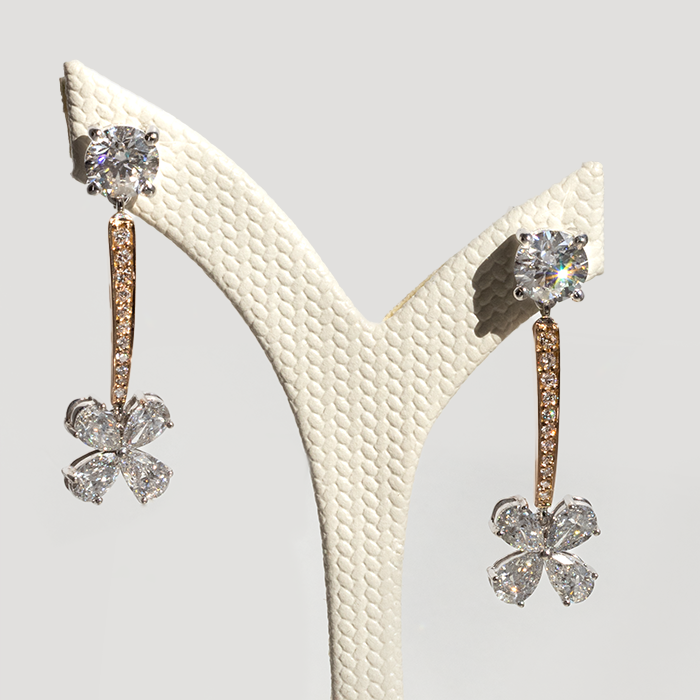 A pair of Danielle Drop Diamond Earrings with round and pear cut diamonds, featuring a rose gold pave stem and a floral motif, displayed on a mannequin.