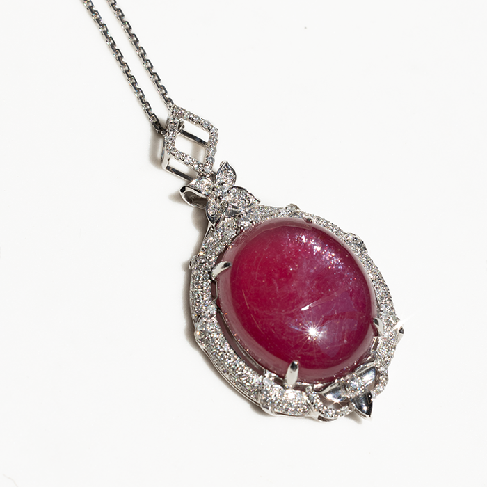 pendant with a cabochon ruby cener stone with micro-pave halo diamonds on the outside