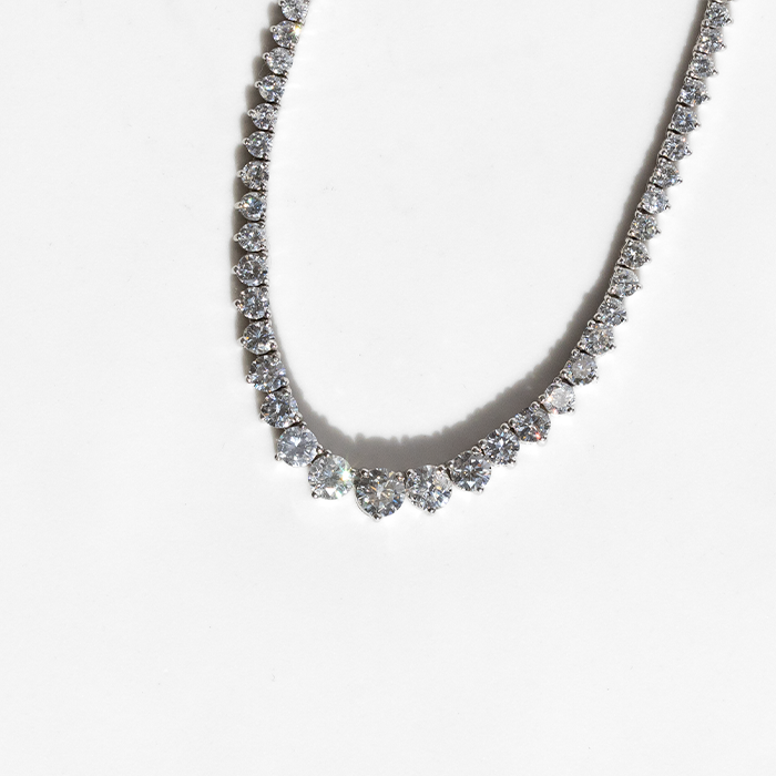A tennis necklace featuring a row of round-cut diamonds set in white gold, displayed against a white background.