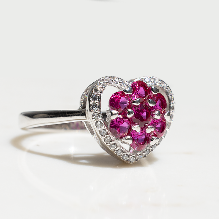A heart-shaped ring with a cluster of red ruby stones in the center and white diamond stones around the halo, set in white gold or platinum.