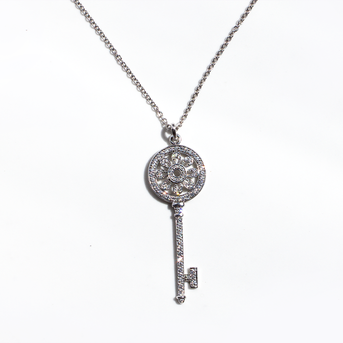 A white gold pendant necklace with a key design and diamond accents, displayed against a neutral background.