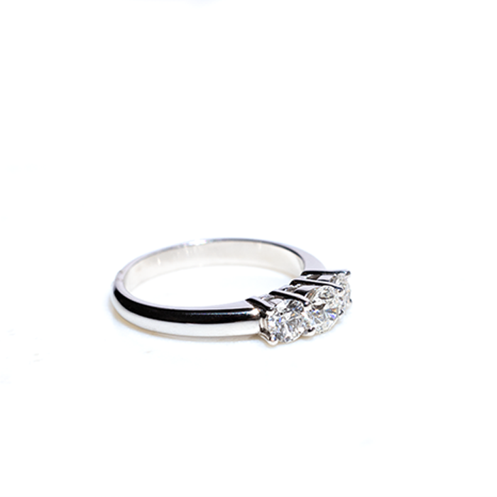 A three-stone diamond ring with the central stone set in a white gold band, accompanied by two smaller round brilliant-cut diamonds on either side.