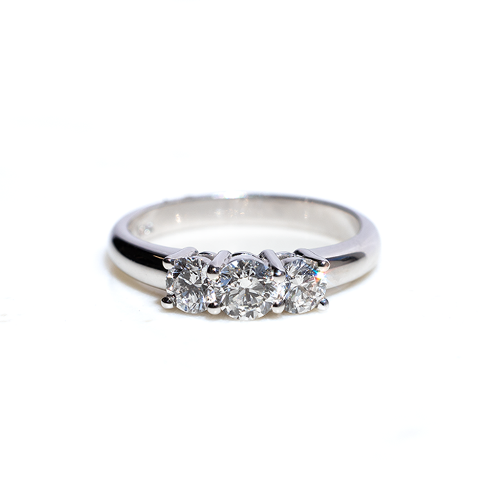 A three-stone diamond ring with the central stone set in a white gold band, accompanied by two smaller round brilliant-cut diamonds on either side.