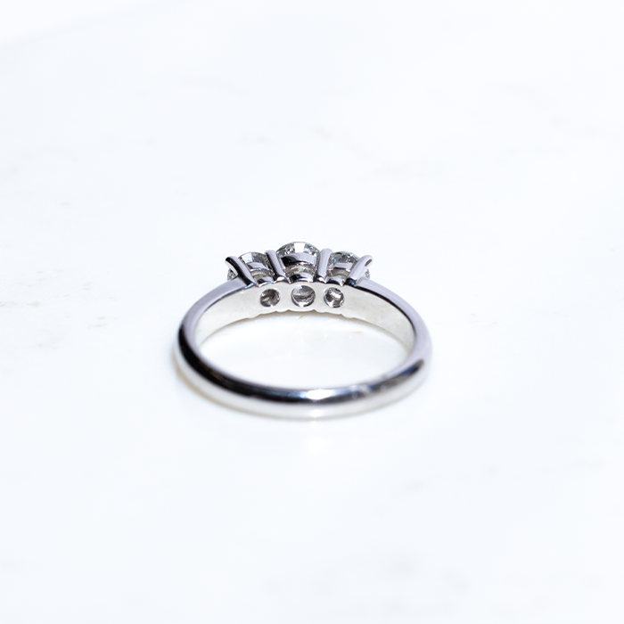 A three-stone diamond ring with the central stone set in a white gold band, accompanied by two smaller round brilliant-cut diamonds on either side.