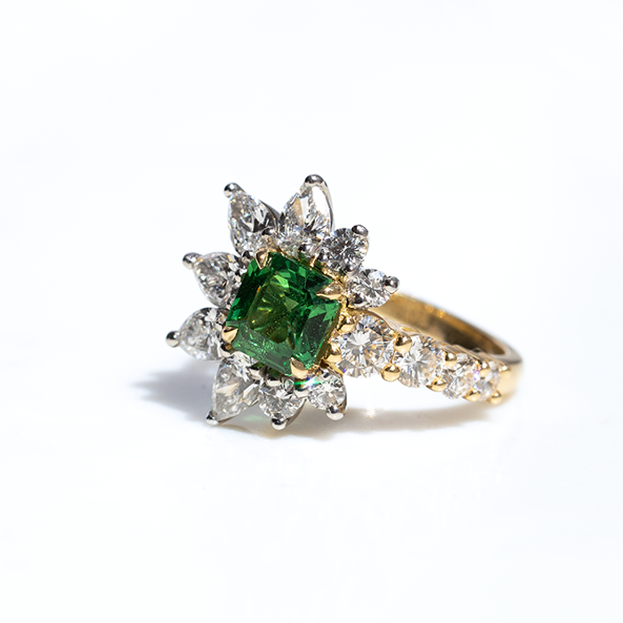 An asymmetric tsavorite and diamond ring with a gold band, featuring a prominent green tsavorite cut in an octagonal shape, flanked by smaller round brilliant cut diamonds.