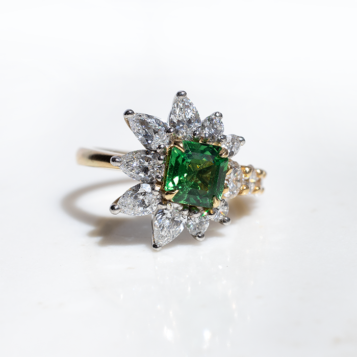 An asymmetric tsavorite and diamond ring with a gold band, featuring a prominent green tsavorite cut in an octagonal shape, flanked by smaller round brilliant cut diamonds.