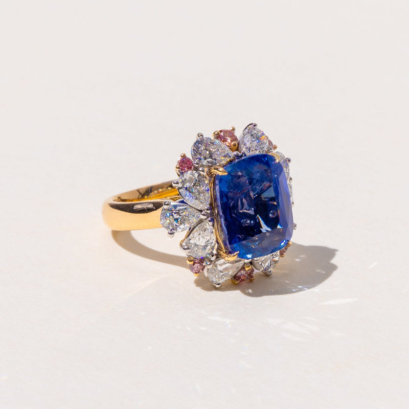 A cushion cut sapphire halo cluster ring with pear-shaped and round brilliant cut diamonds set in 18K yellow and white gold.