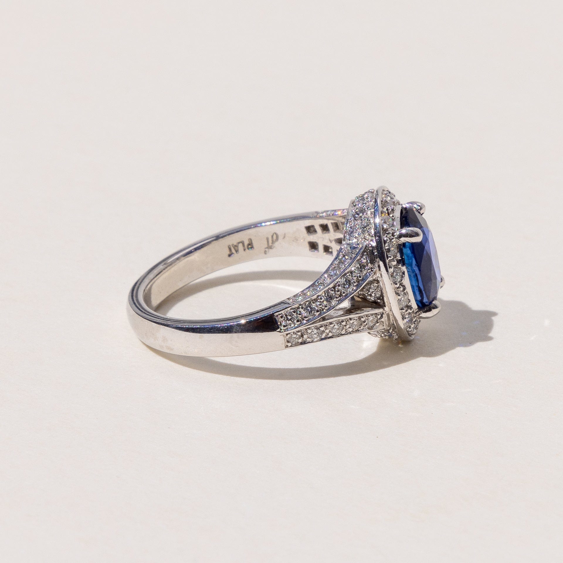 An oval blue sapphire halo ring with a split band and round brilliant cut diamonds, set in platinum.