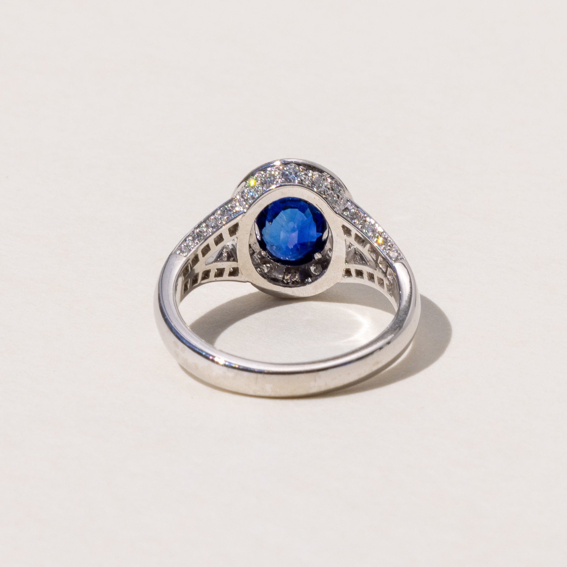 An oval blue sapphire halo ring with a split band and round brilliant cut diamonds, set in platinum.