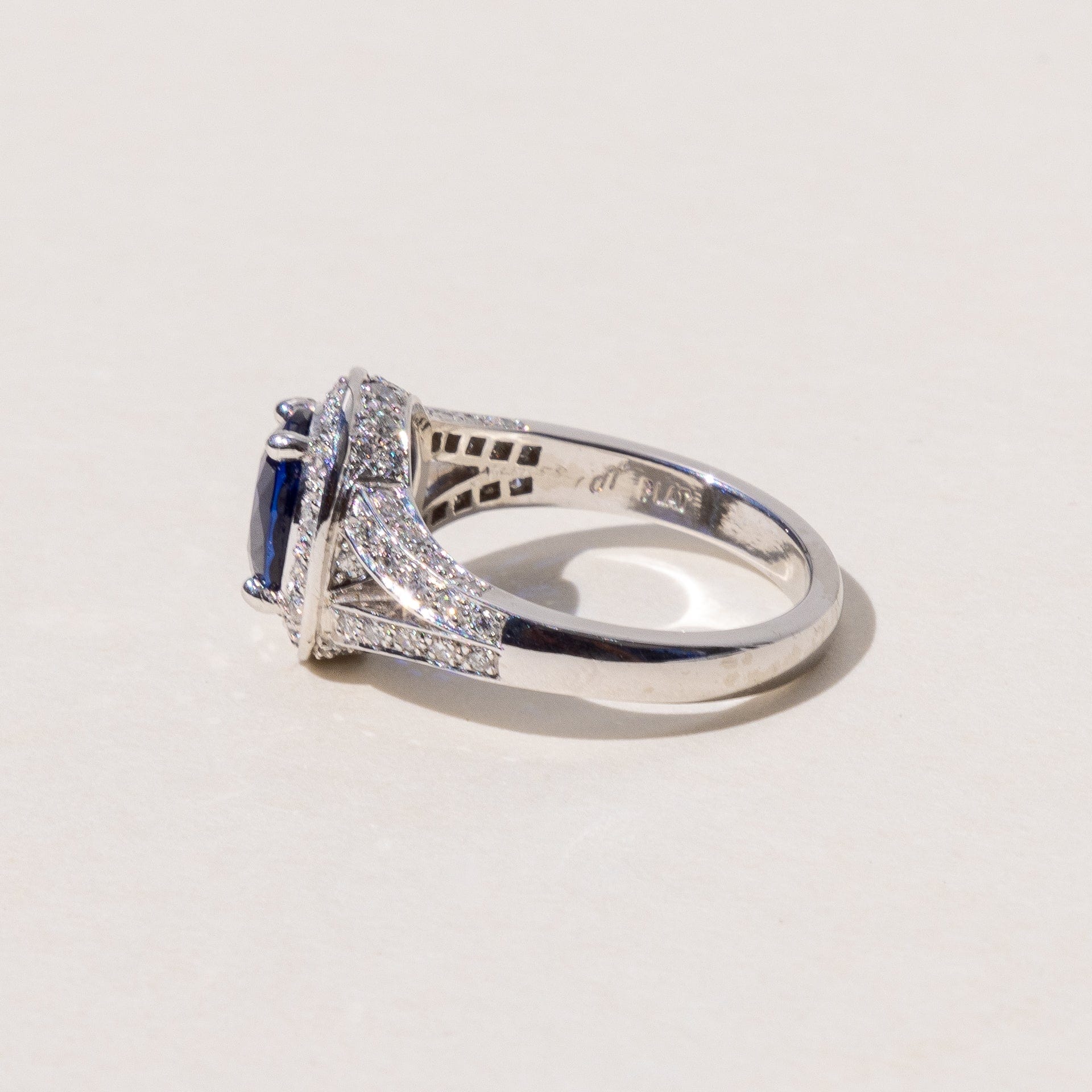 An oval blue sapphire halo ring with a split band and round brilliant cut diamonds, set in platinum.