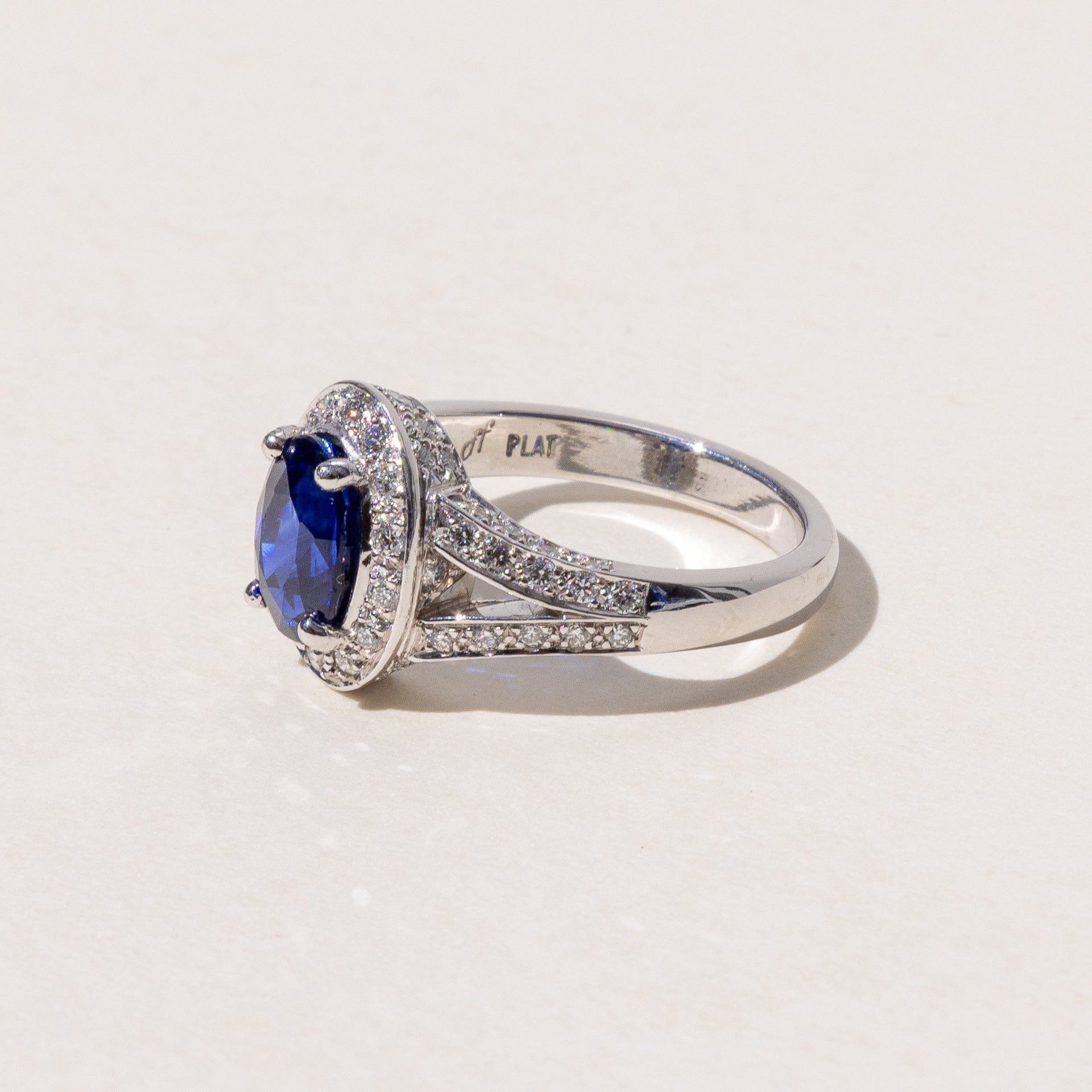 An oval blue sapphire halo ring with a split band and round brilliant cut diamonds, set in platinum.