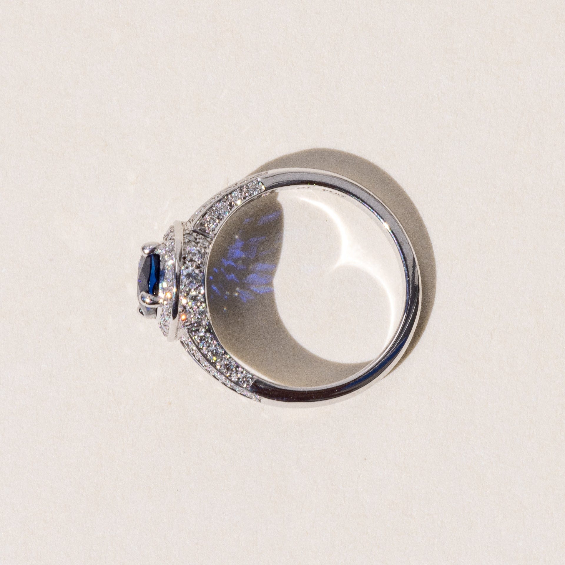 An oval blue sapphire halo ring with a split band and round brilliant cut diamonds, set in platinum.