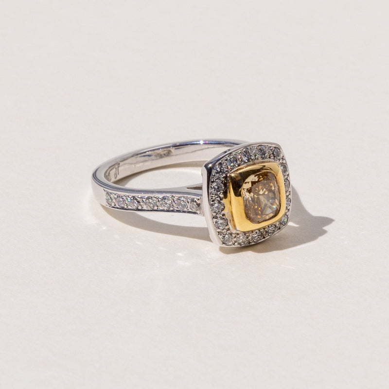 A square cushion cut cognac diamond halo ring with round brilliant cut diamonds around it, set in yellow and white gold.