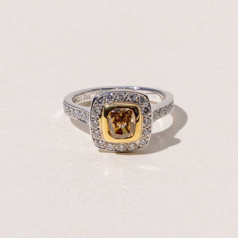A cushion cut cognac diamond halo ring with round brilliant cut diamonds around it, set in yellow and white gold.