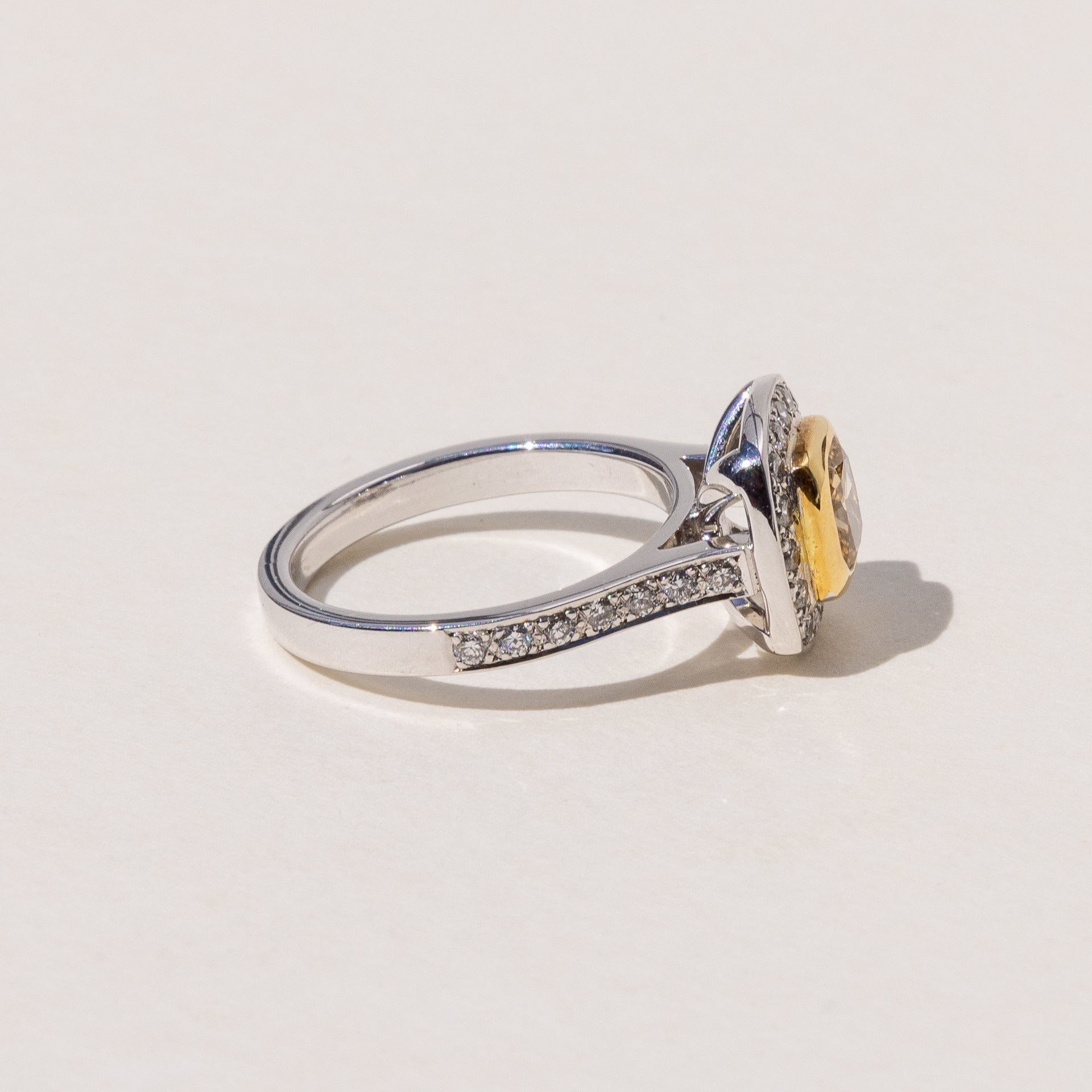 A cushion cut cognac diamond halo ring with round brilliant cut diamonds around it, set in yellow and white gold.