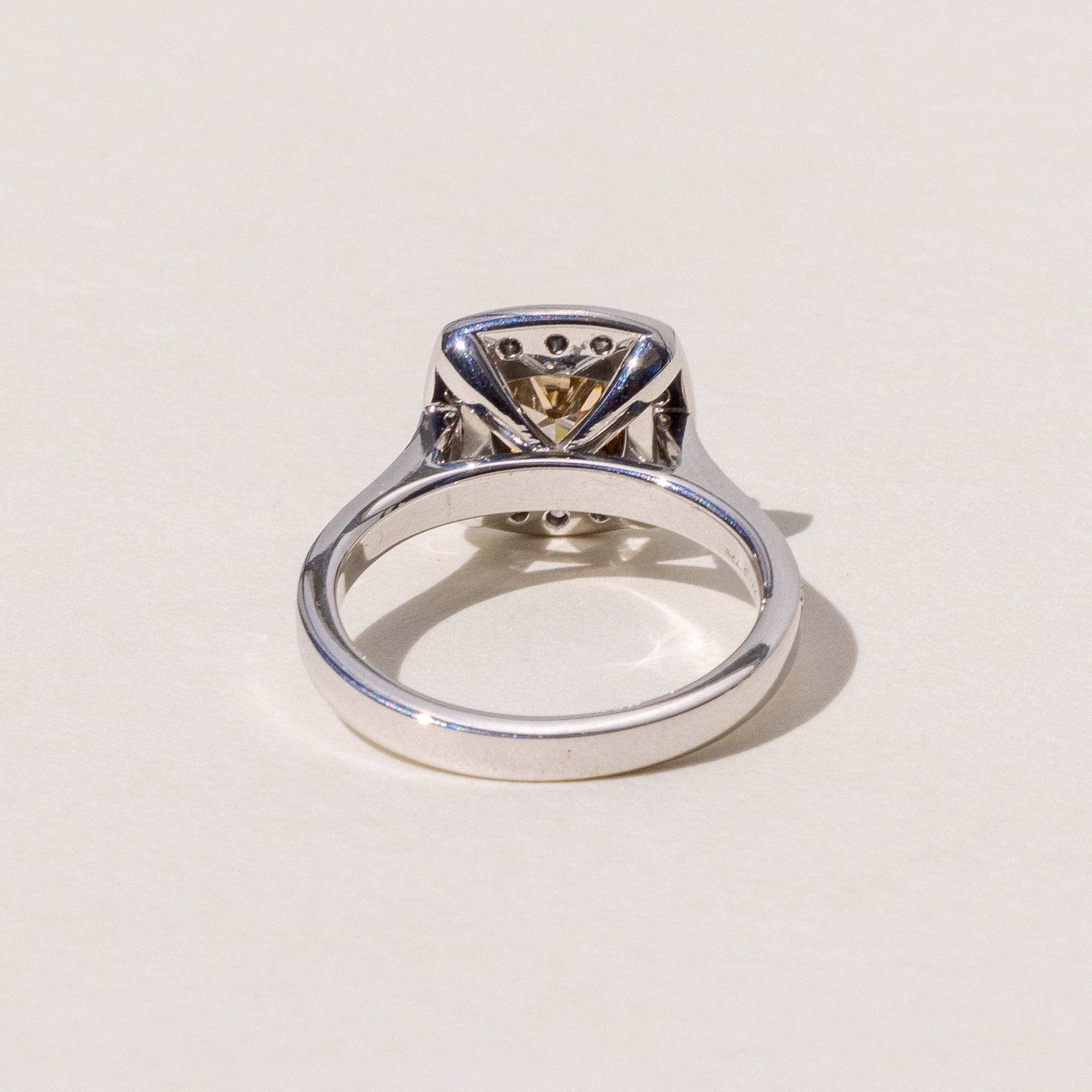 A cushion cut cognac diamond halo ring with round brilliant cut diamonds around it, set in yellow and white gold.