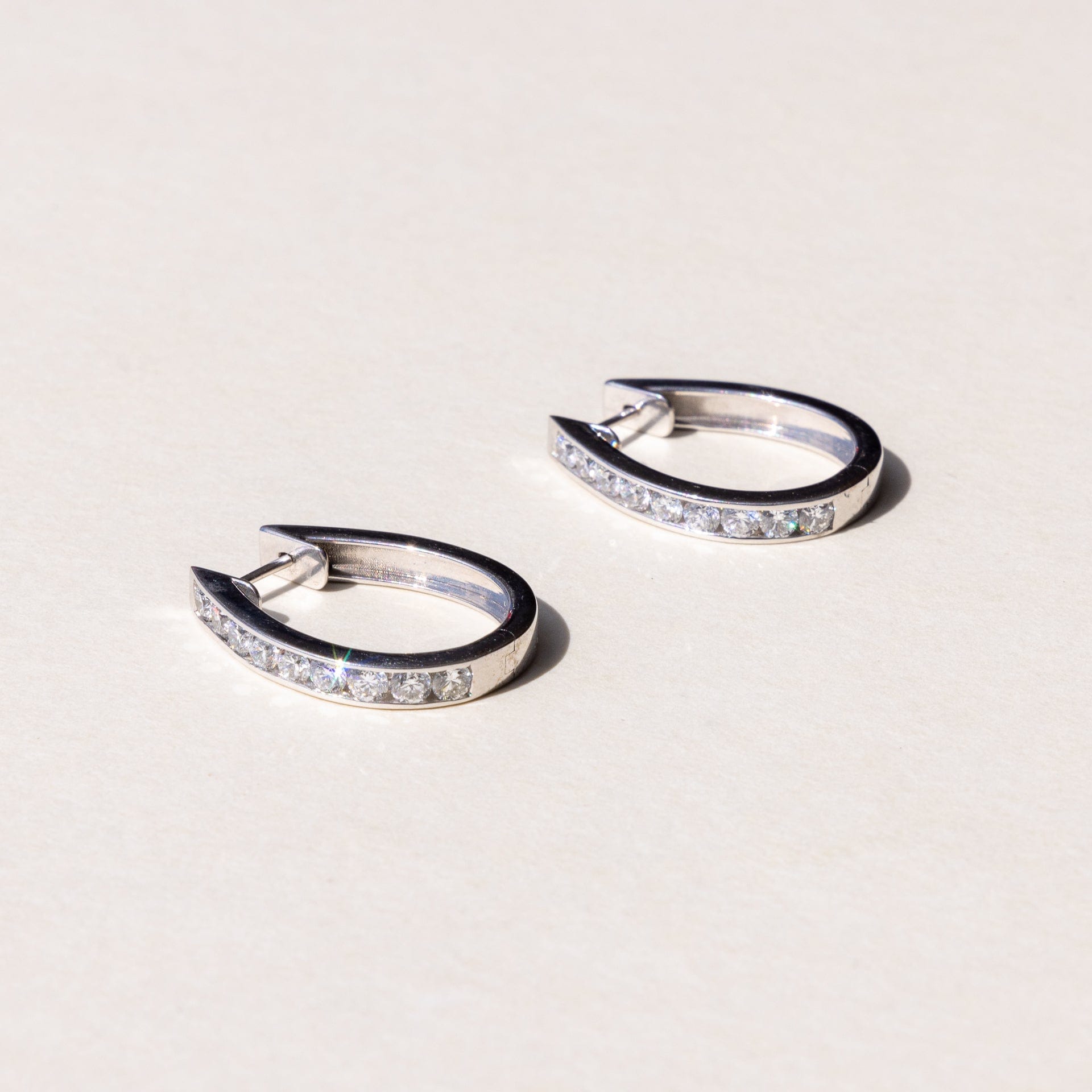 A pair of white gold hoop earrings with a row of round brilliant cut diamonds set across the hoop.
