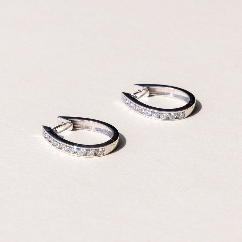 A pair of white gold hoop earrings with a row of round brilliant cut diamonds set across the hoop.