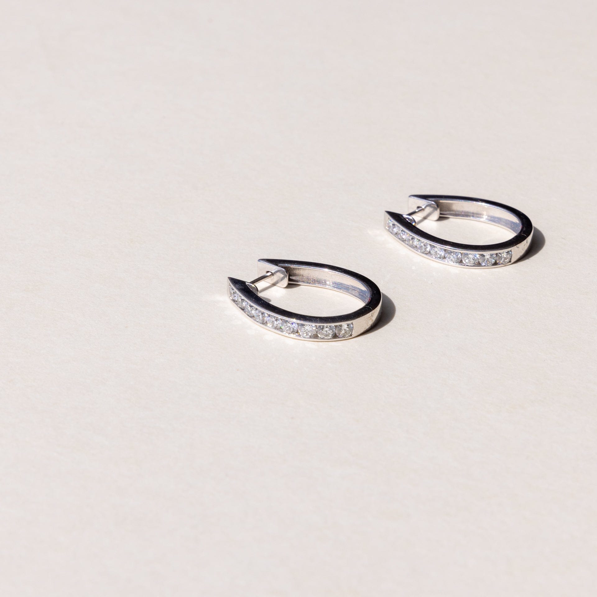A pair of white gold hoop earrings with a row of round brilliant cut diamonds set across the hoop.