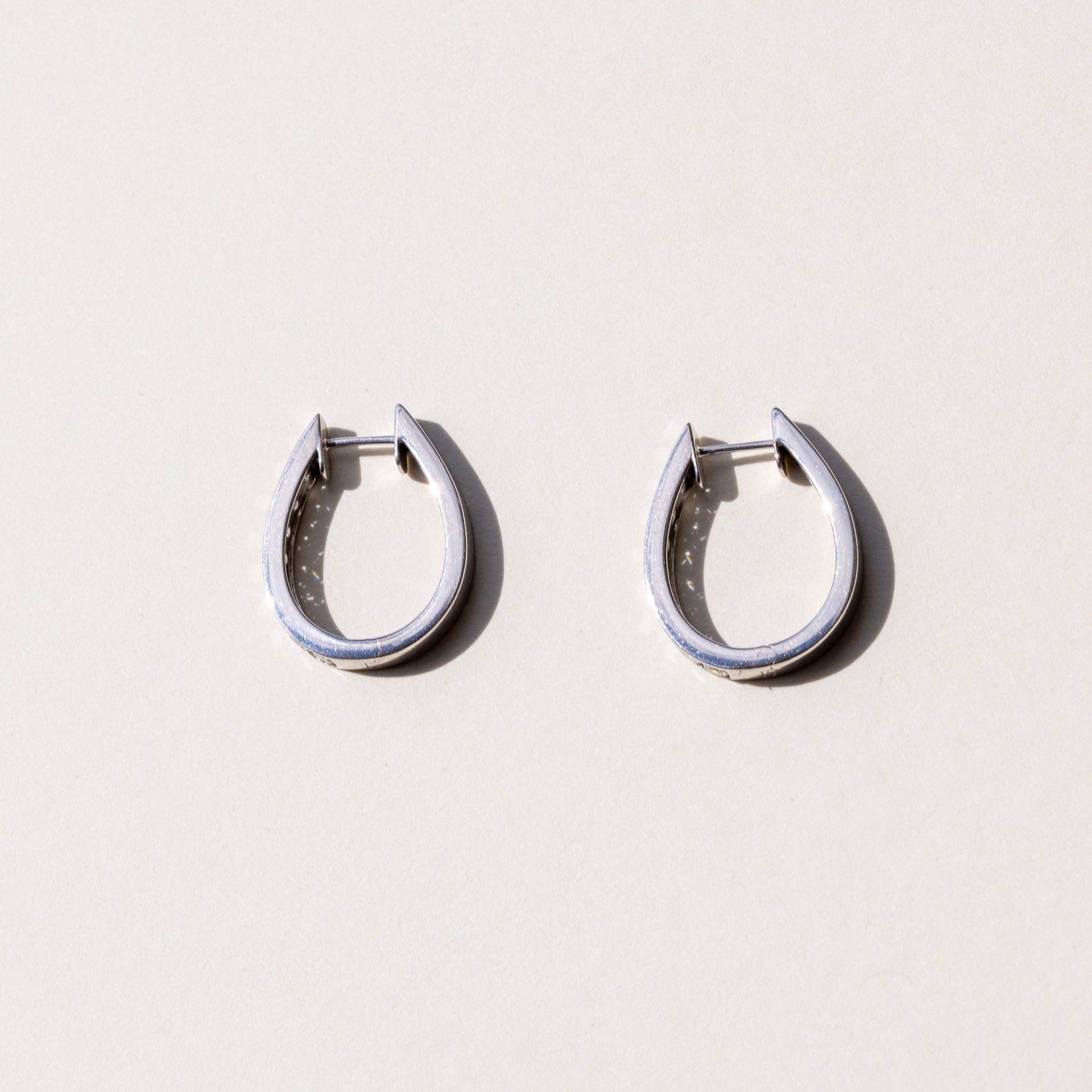 A pair of white gold hoop earrings with a row of round brilliant cut diamonds set across the hoop.
