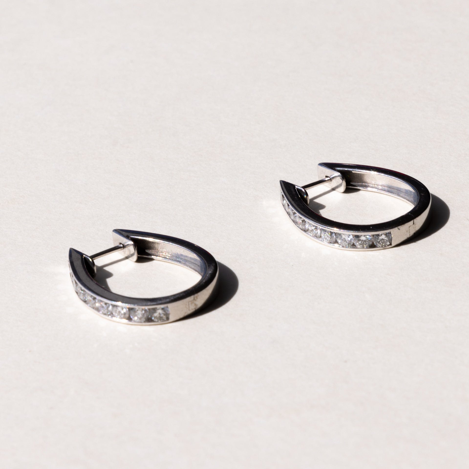 A pair of white gold hoop earrings with a row of round brilliant cut diamonds set across the hoop.
