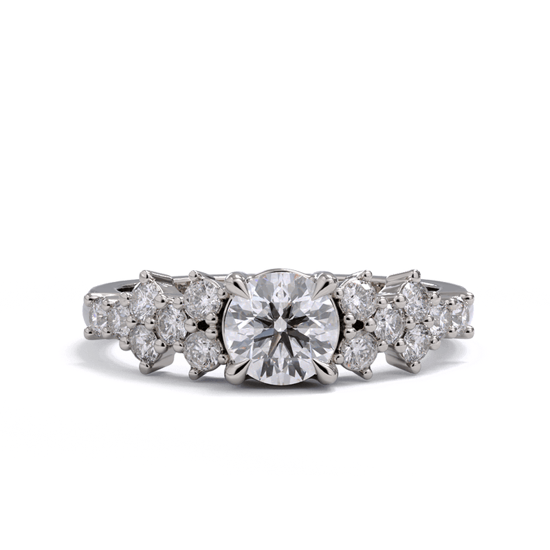 A white gold or platinum engagement ring with a round diamond center stone and clusters of round diamonds on each side. Pave diamonds down the side of band.
