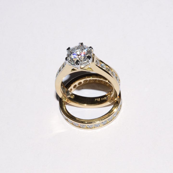 A wedding set featuring a round brilliant diamond solitaire in an 18ct yellow gold eternity band, with additional round brilliant diamonds set around the main stone.