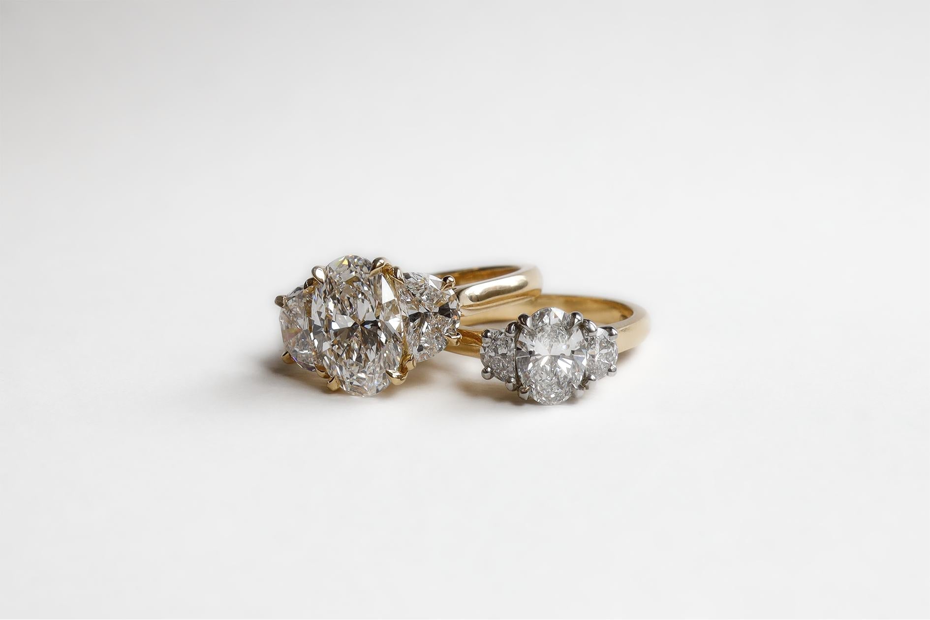 Two diamond rings that feature an oval center stone and two hald moons. One is made in Gold and the other in Platinum and Gold 