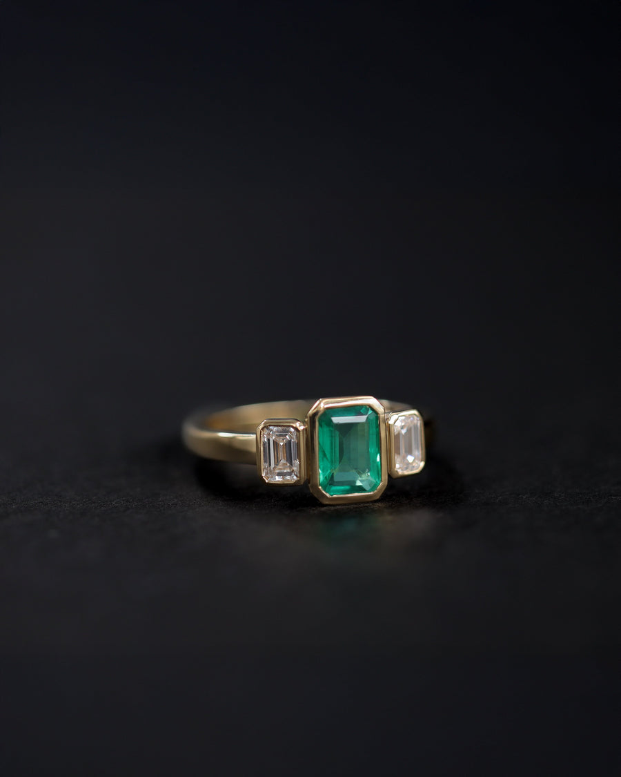 Bezel set 3 stone engagement ring with a vibrant emerald center stone, flanked by two emerald cut diamonds. Handmade in Auckland, New Zealand by award winning master jewellers 