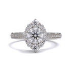 A gold diamond ring with a large round central diamond surrounded by a halo of smaller round diamonds. Set in platinum on a platinum or white gold band with pave down on the band, displayed against a white background.