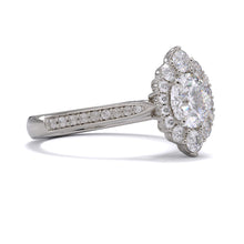 A gold diamond ring with a large round central diamond surrounded by a halo of smaller round diamonds. Set in platinum on a platinum or white gold band with pave down on the band, displayed against a white background.