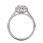 A gold diamond ring with a large round central diamond surrounded by a halo of smaller round diamonds. Set in platinum on a platinum or white gold band with pave down on the band, displayed against a white background.