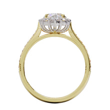A gold diamond ring with a large round central diamond surrounded by a halo of smaller round diamonds. Set in platinum on a yellow gold band with pave down on the band, displayed against a white background.