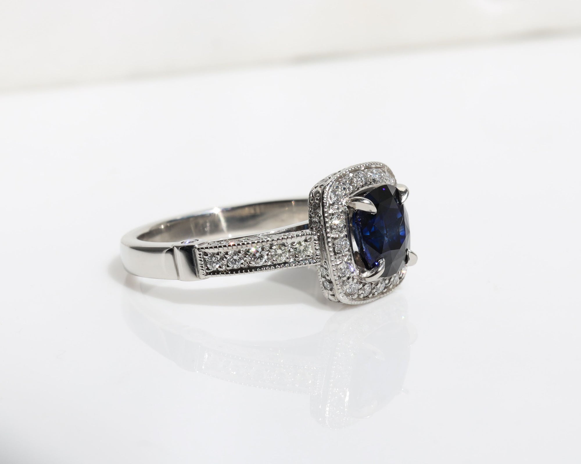 Handmade ring featuring a blue sapphire centre stone, surrounded by a halo of diamonds, with a pavé diamond band.
