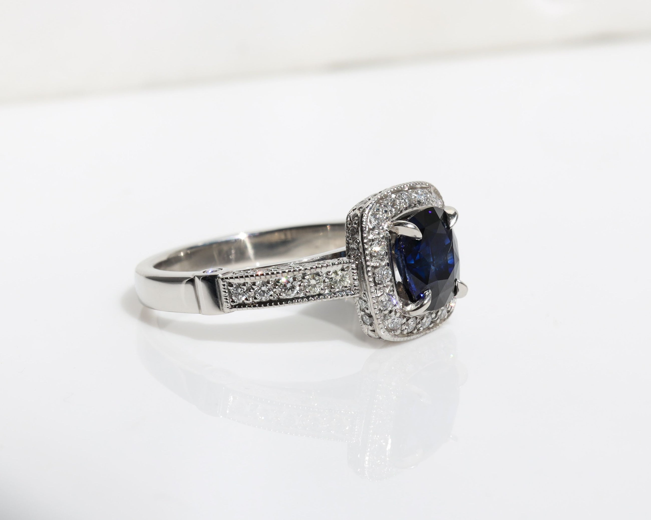 Handmade ring featuring a blue sapphire centre stone, surrounded by a halo of diamonds, with a pavé diamond band.