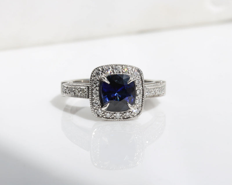 Handmade ring featuring a blue sapphire centre stone, surrounded by a halo of diamonds, with a pavé diamond band.
