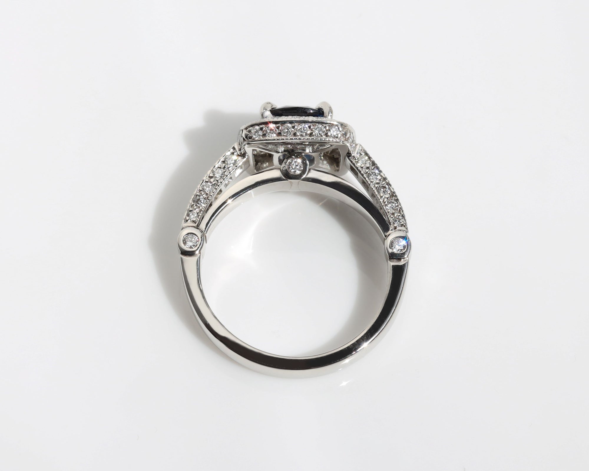 Handmade ring featuring a blue sapphire centre stone, surrounded by a halo of diamonds, with a pavé diamond band.